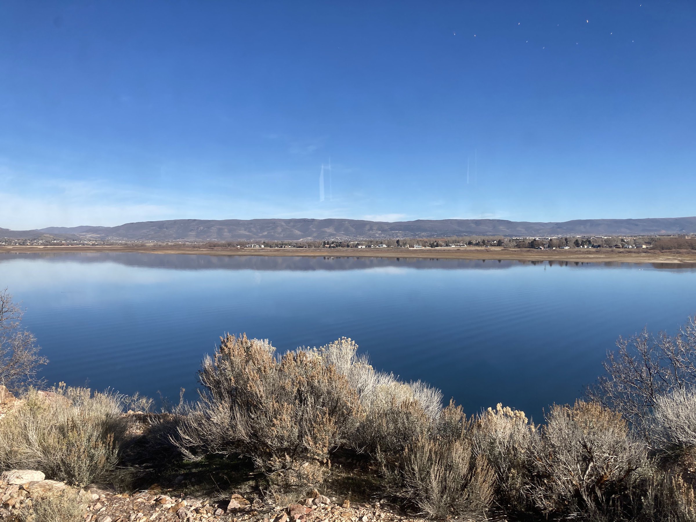 Deer Creek Reservoir, still and deep blue under a clear sky, with sagebrush in front