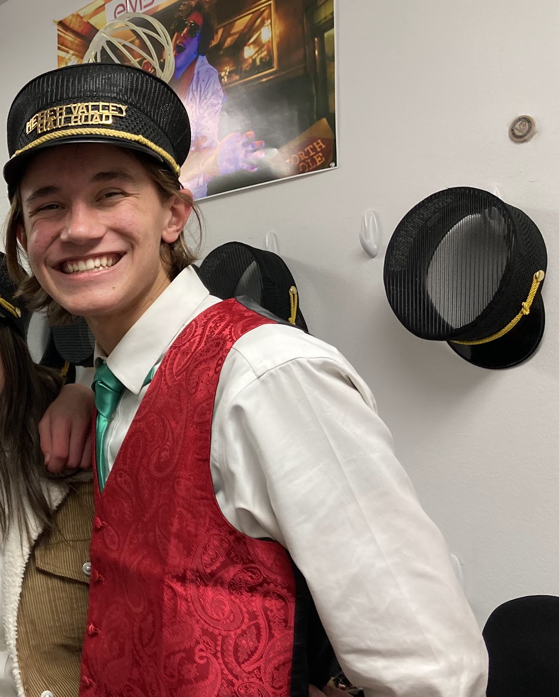 Ethan smiling in a red brocade vest, white shirt, green tie and a Heber Valley Railroad cap
