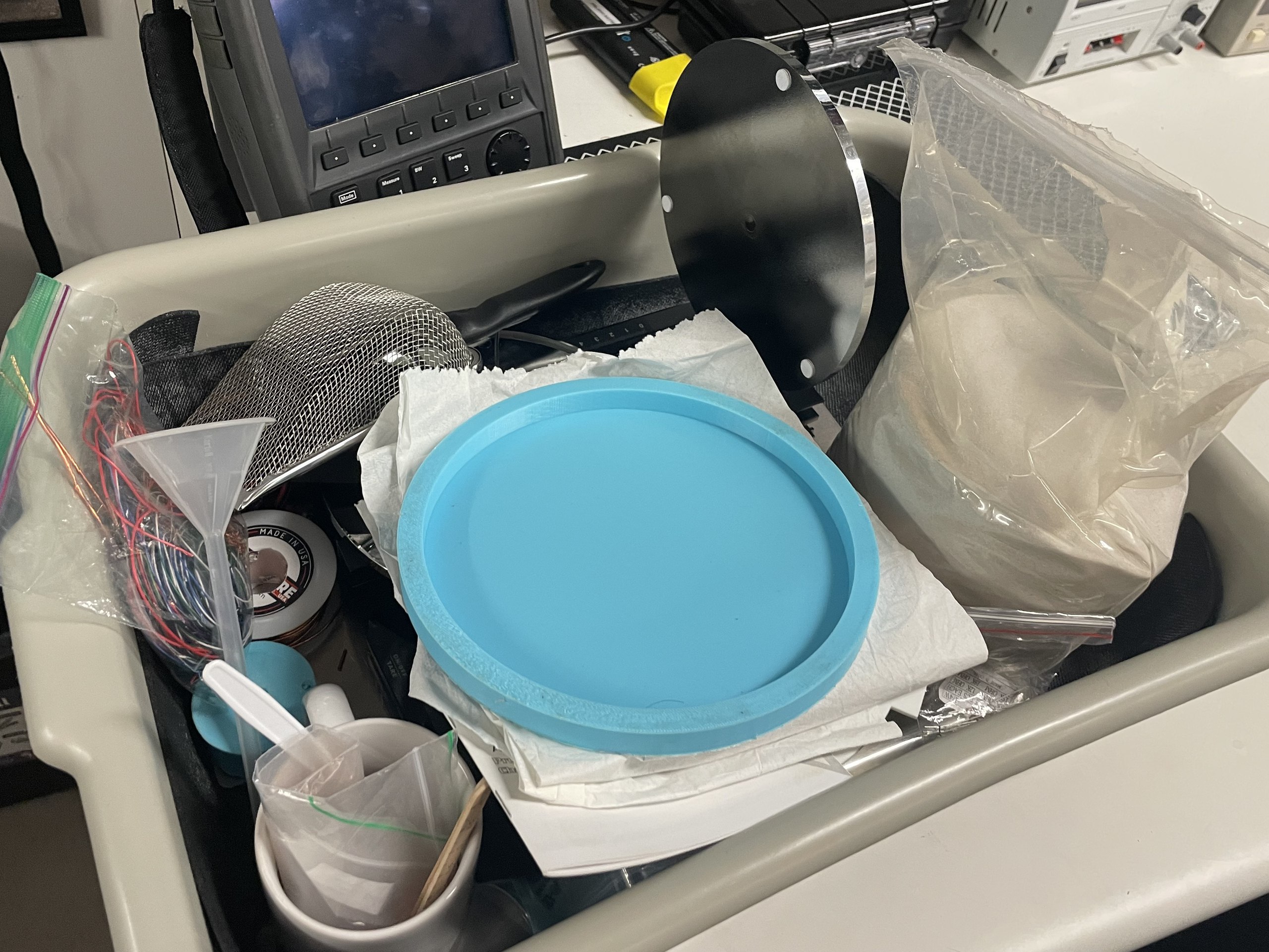 A bin of sample supplies in the Radio Glaciology Lab: a bag of sand, copper wire, a funnel and a sieve